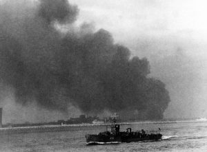 A picture of troops aboard a rescue ship while Dunkirk burns in the background