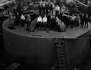 A picture of people standing on one of the 2 million-pound hydroelectric generators for the dam=construction of the Hoover Dam
