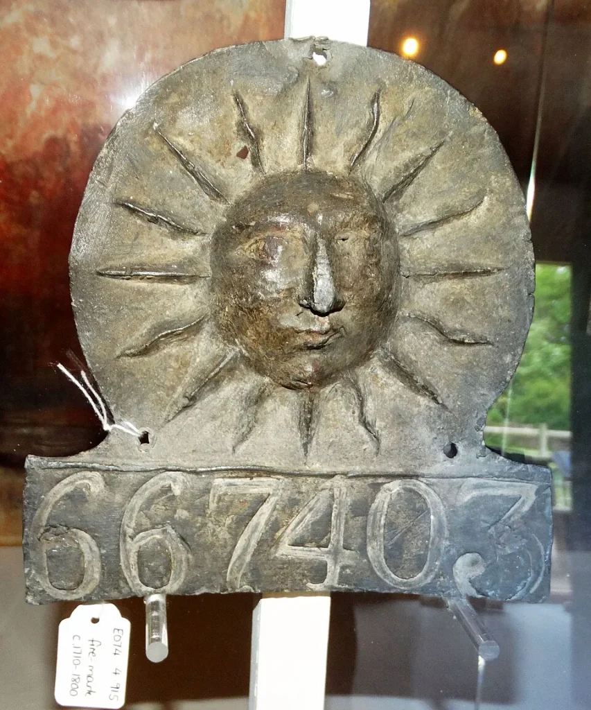 Close-up photograph of a Sun Fire Office insurance mark, a decorative metal plaque with a radiating sun face and lettering, mounted on a wall.